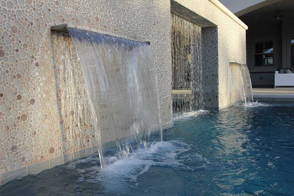 A water wall with two scuppers and a rain curtain pours into a custom swimming pool designed and built by Paradise Pools & Spas..