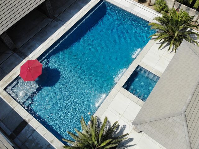 From the Paradise Pools & Spas Galleries: Massive swimming pool with spa and red umbrella.